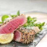 Plate of seared ahi tuna garnished with fresh herbs and served with a side of colorful vegetables