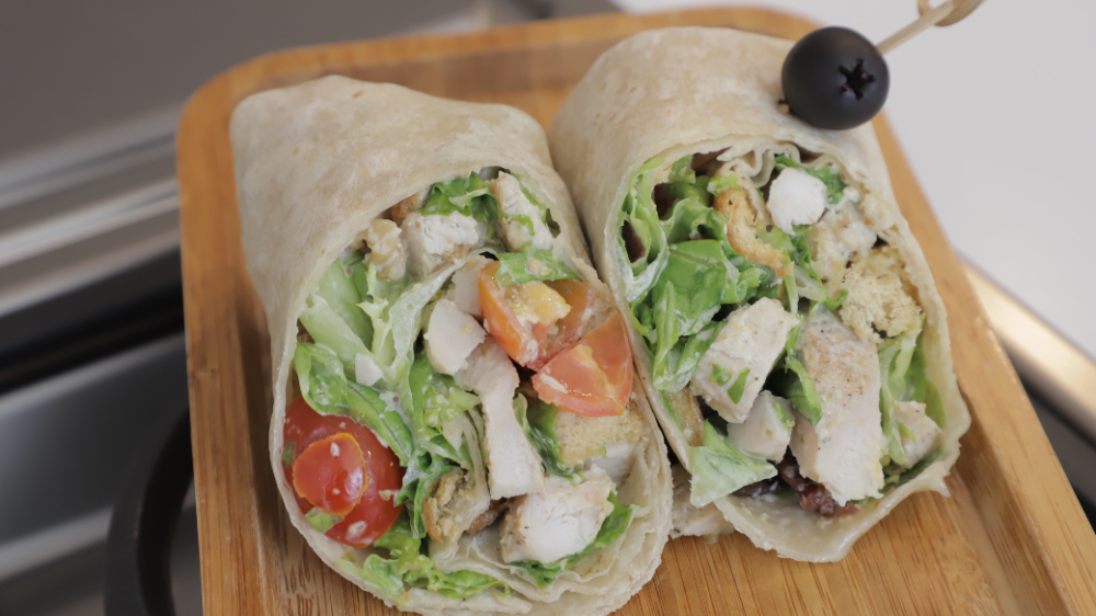 A delicious turkey cranberry wrap filled with sliced turkey, fresh spinach, and a generous spread of cranberry sauce, all wrapped in a whole grain tortilla, served on a wooden cutting board.