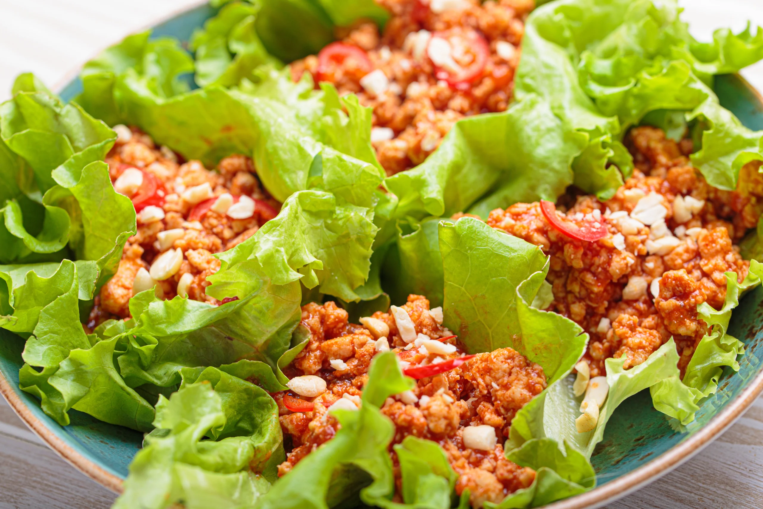 Fresh Thai turkey lettuce wraps featuring crisp lettuce leaves filled with savory ground turkey, colorful vegetables, and drizzled with a tangy peanut or chili sauce, garnished with fresh herbs like cilantro and lime wedges.