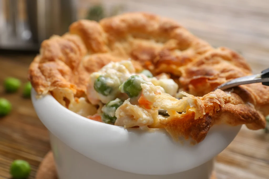 A steaming turkey pot pie with biscuits, showcasing a golden-brown flaky crust and hearty filling, served fresh from the oven on a rustic wooden table.