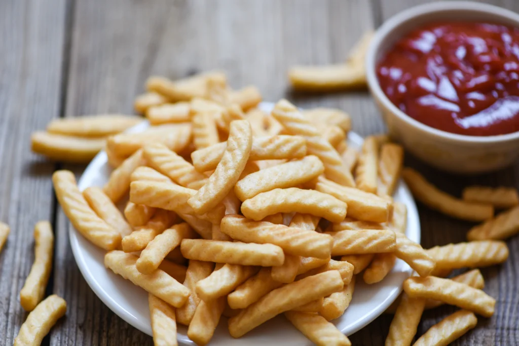 A plate of golden-brown crinkle fries served with a side of ketchup, showcasing their crispy texture and wavy shape.