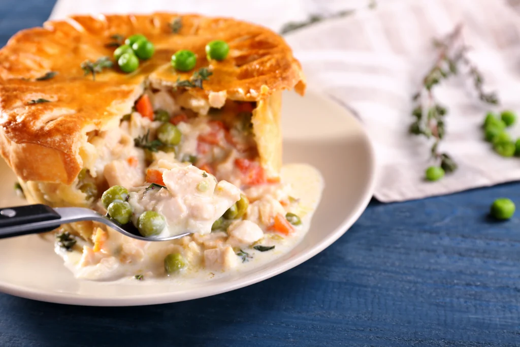 A steaming turkey pot pie with biscuits, showcasing a golden-brown flaky crust and hearty filling, served fresh from the oven on a rustic wooden table.