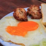 "A hearty breakfast plate featuring scrambled eggs, golden-brown grilled chicken, and a side of fresh vegetables, served on a white plate with a sprinkle of herbs."