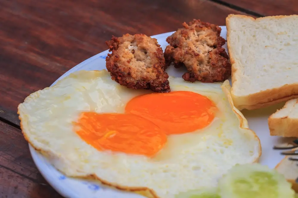 "A hearty breakfast plate featuring scrambled eggs, golden-brown grilled chicken, and a side of fresh vegetables, served on a white plate with a sprinkle of herbs."