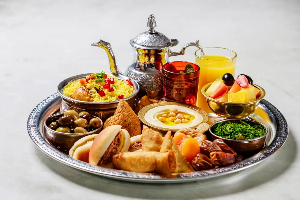 A colorful Arabic breakfast spread featuring a plate of Ful Medames made with fava beans, garlic, and lemon, served with warm pita bread. Accompanying the dish is creamy Labneh topped with olive oil and za'atar, alongside fresh vegetables and olives. Sweet Baklava drizzled with honey, fresh fruit, and a bowl of honey-sweetened porridge complete the meal, showcasing a delightful mix of flavors and textures.